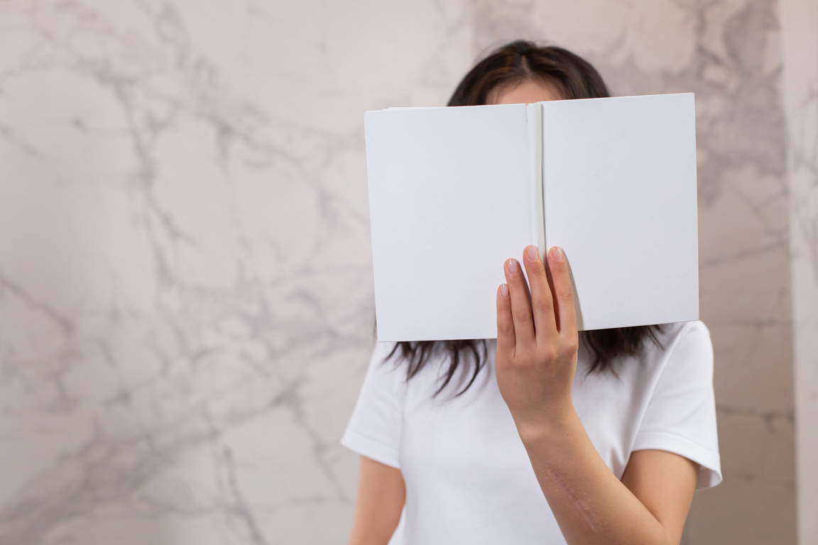 Faceless woman covering face with blank book